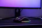 Altec Lansing GM300 black gaming mouse with rainbow RGB underglow on dark gaming desk with glowing monitor in background