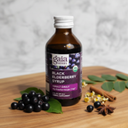 Gaia Herbs Black Elderberry Syrup bottle on a natural wood surface with elderberries and herbal styling