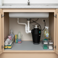 Compact black garbage disposal neatly installed under kitchen sink with plumbing and power cord connected