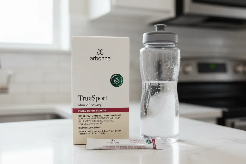 Arbonne TrueSport Muscle Recovery box on kitchen counter with water bottle and stick pack fitness lifestyle