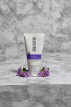 Rodan and Fields UNBLEMISH Invisible Matte Defense SPF 30 tube on white marble with soft purple accent flowers, premium studio skincare photography – More4less Outlet