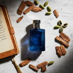 Flat-lay of blue fragrance bottle with cedarwood chips and cardamom pods on marble surface