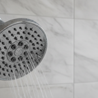 Macro shot of round chrome showerhead nozzle face against light grey marble tiles