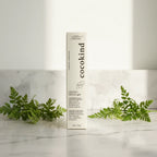 Cocokind Beginner Retinol Gel white treatment box with fresh green plants on white marble background, warm soft window light