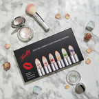 Flat lay of Firstfly Gold Foil Flowers lipstick array on white marble with decorative cosmetic tools