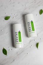 Professional flat lay of green and white skincare bottles on a clean neutral marble background