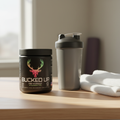 Bucked Up Original Strawberry Kiwi pre-workout container on a countertop beside a shaker bottle and towel
