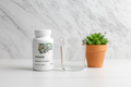 Thorne supplement bottle on clean neutral surface next to glass of water and succulent