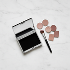Lifestyle image - silver clamshell makeup organizer case open with eyeshadow pans and brush on desk, editorial flatlay for visual context only