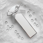 Lifestyle image — white and silver slim perfume wand box on white tissue paper with silver ribbon bow and scattered crystals, luxurious gifting flatlay for visual context only