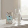 Gillette Venus Pubic Hair & Skin Razor Kit on white marble vanity top with glass carafe of water