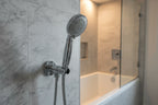 Staged residential bathroom detail with polished chrome handheld shower head resting in wall bracket