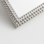 Close-up of an elegant silver-tone beaded picture frame detail on a white surface