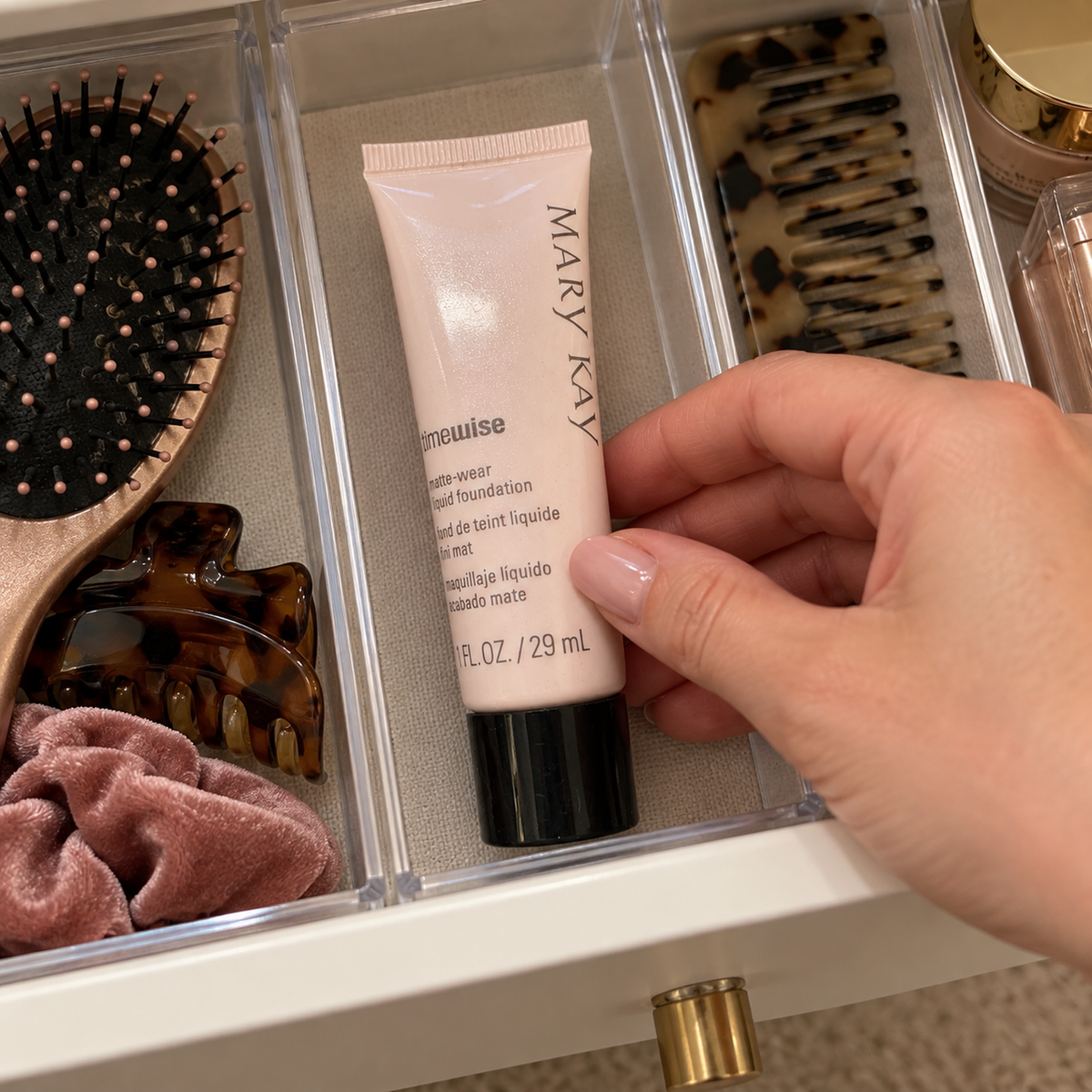 A hand places a capped Mary Kay TimeWise Matte-Wear foundation tube in a vanity drawer divider.