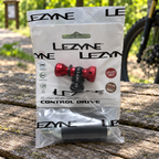 Packaged red Lezyne Control Drive CO2 inflator and 16g cartridge on a picnic table at a cycling trailhead; AI-staged lifestyle composite.