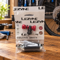 Red Lezyne Control Drive CO2 inflator and 16g cartridge in original package on a bicycle maintenance workbench; AI-staged lifestyle composite.