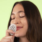 Woman holding a Lifelines Pebbles Grounding Stone close to her face.