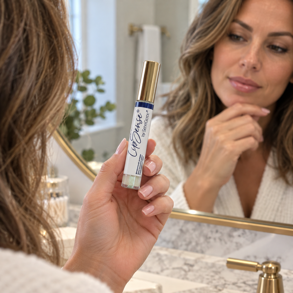 Holding a capped Clover LipSense gloss tube beside a vanity mirror