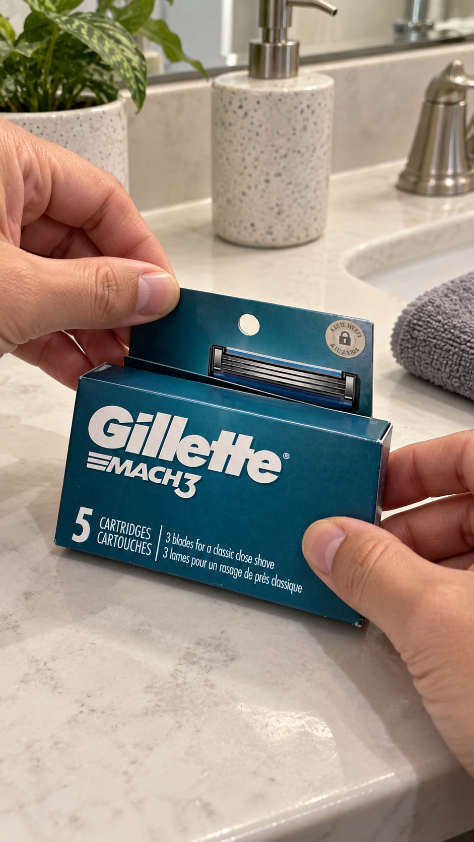 Hands holding a Gillette MACH3 five-cartridge refill pack beside a bathroom sink.