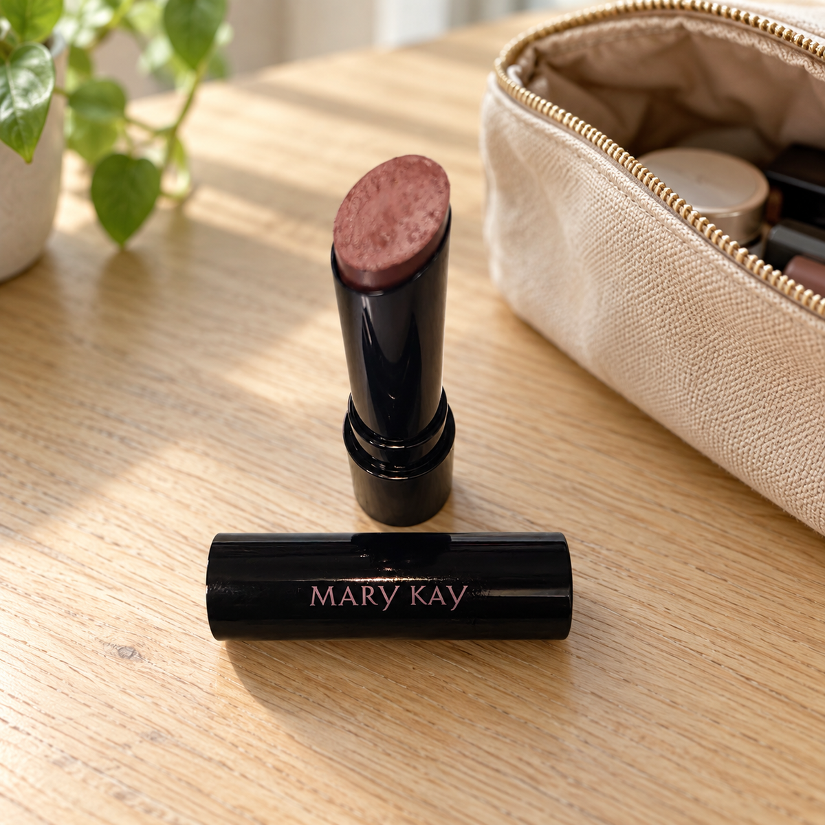 Mary Kay Better Than Bare lipstick beside a beige makeup pouch on a wood tabletop