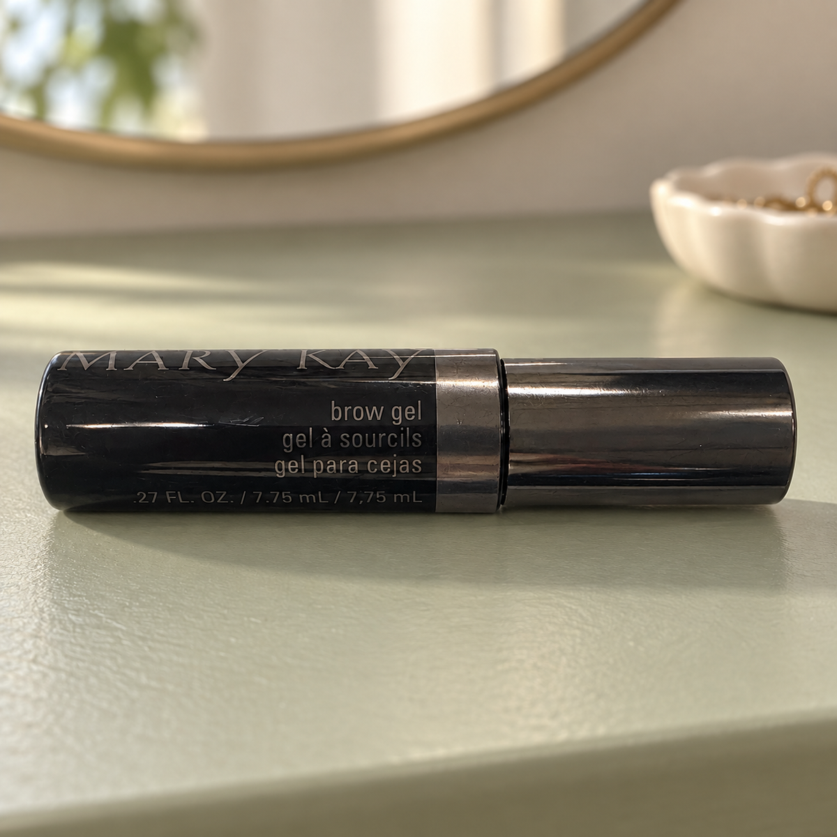Mary Kay Brow Gel black tube on a sage dressing table with a mirror in the background