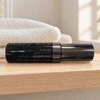 Mary Kay Brow Gel black tube on a wooden bathroom shelf beside folded cream towels