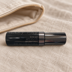 Mary Kay Brow Gel black tube beside a beige canvas travel pouch on linen