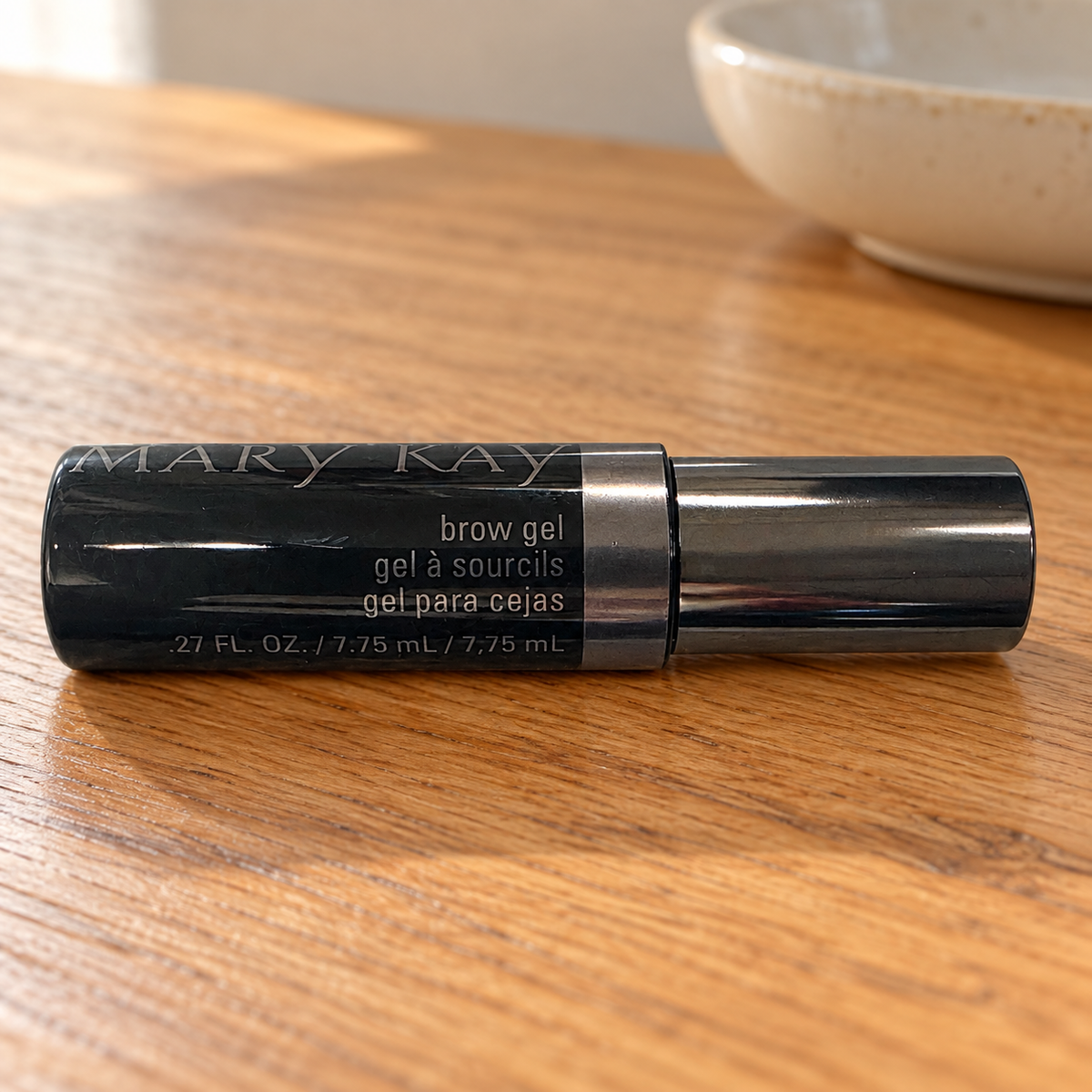 Mary Kay Brow Gel black tube with metallic cap on a warm wooden vanity