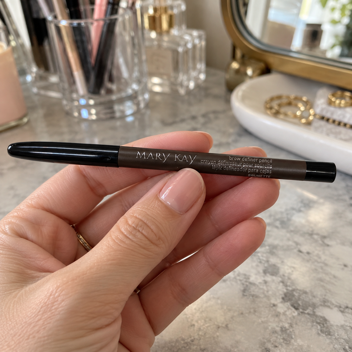 A woman holding a capped Mary Kay Brunette Brow Definer Pencil at her dressing table.