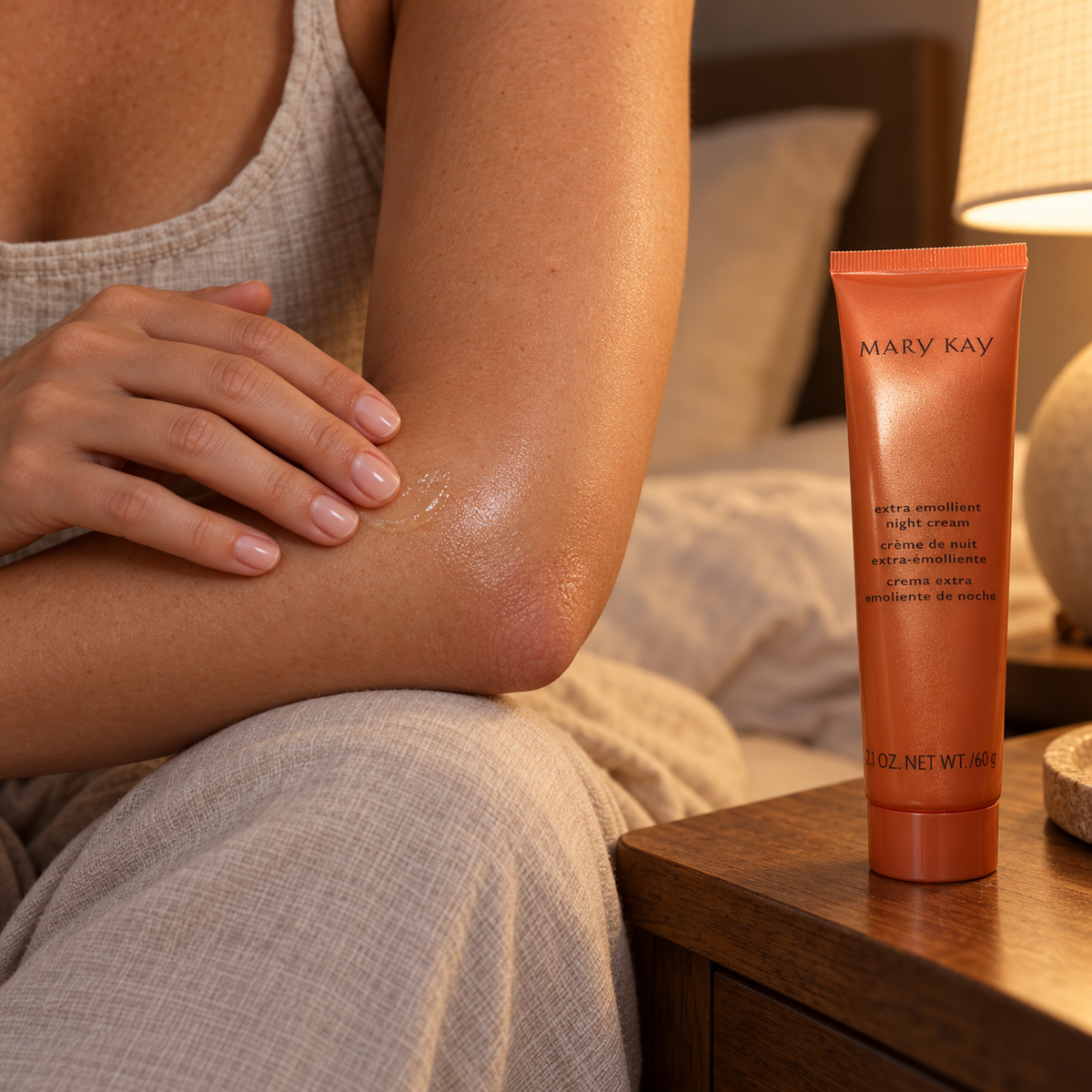 Mary Kay Extra Emollient Night Cream orange tube beside an adult applying a small amount to a bare elbow