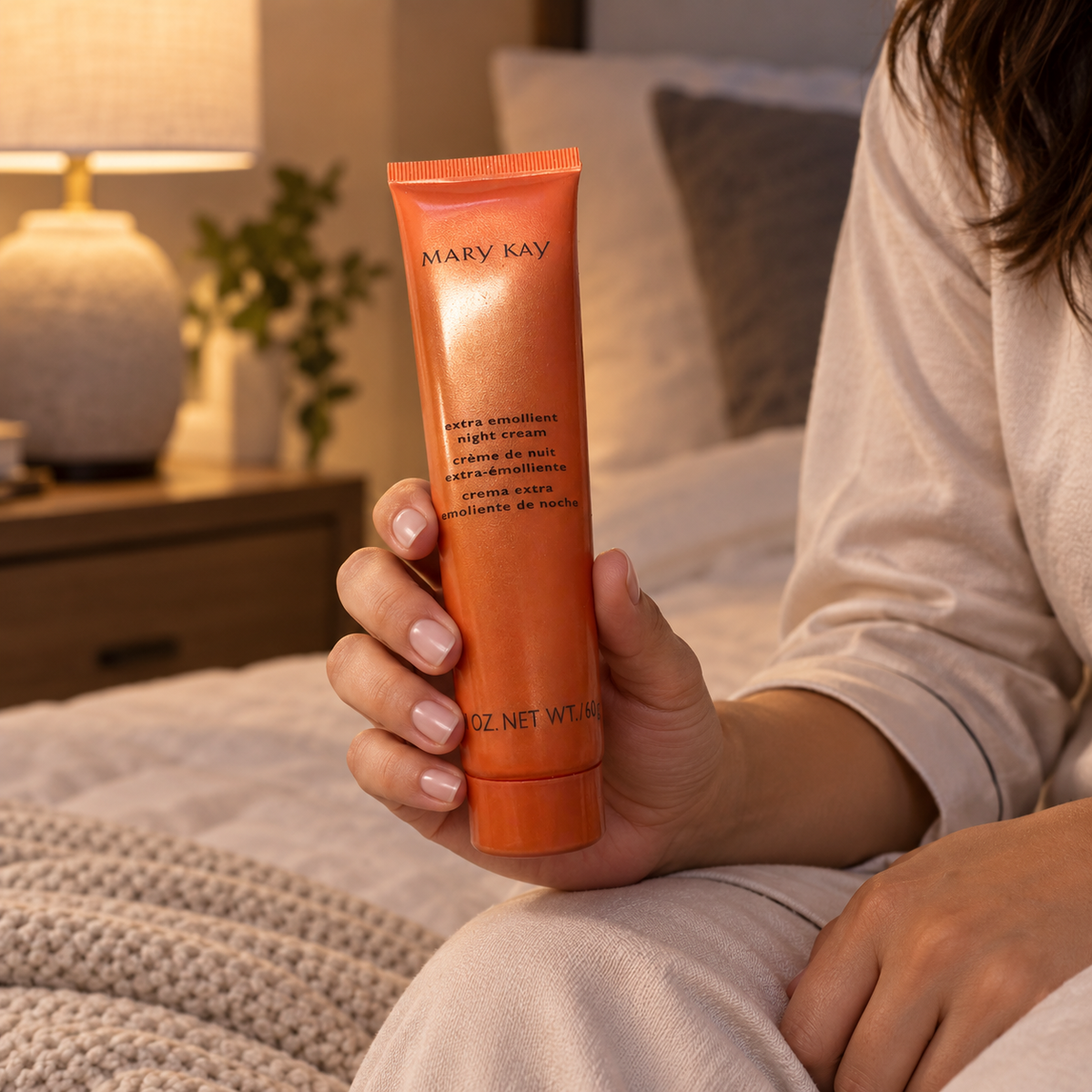 Mary Kay Extra Emollient Night Cream orange 60 g tube held beside a bed