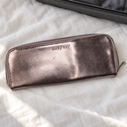 Closed metallic Mary Kay eye brush case on ivory linen beside a suitcase