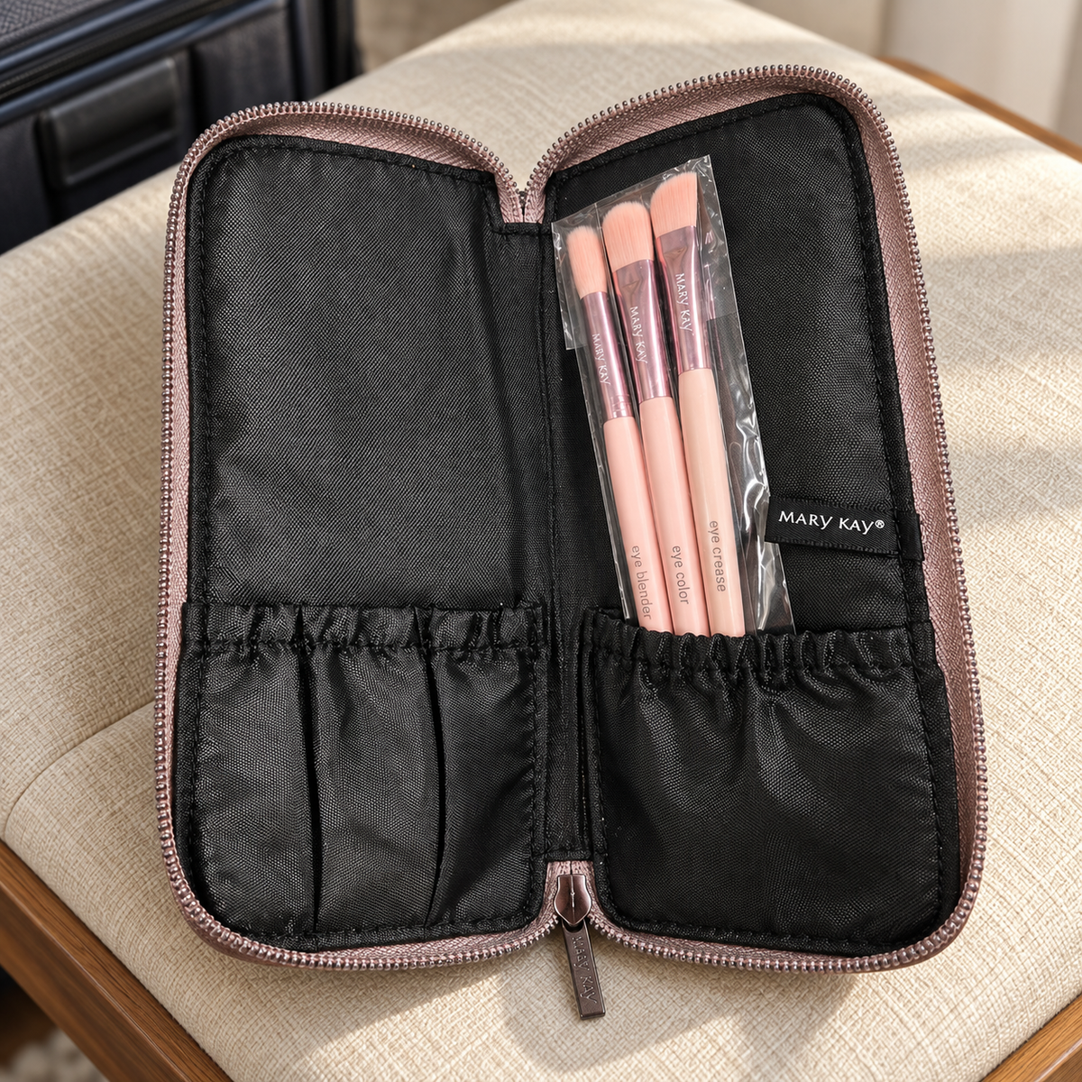 Three sleeved pink Mary Kay eye brushes in the open case on a linen travel bench