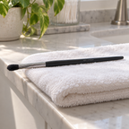 Mary Kay Eye Crease Brush laid flat on a towel with its bristles extending over the counter edge.