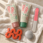 Mary Kay foot-care bundle with pink-cap balm, green-cap soak, nail file, two orange toe separators and sealed pumice stone on an ivory towel