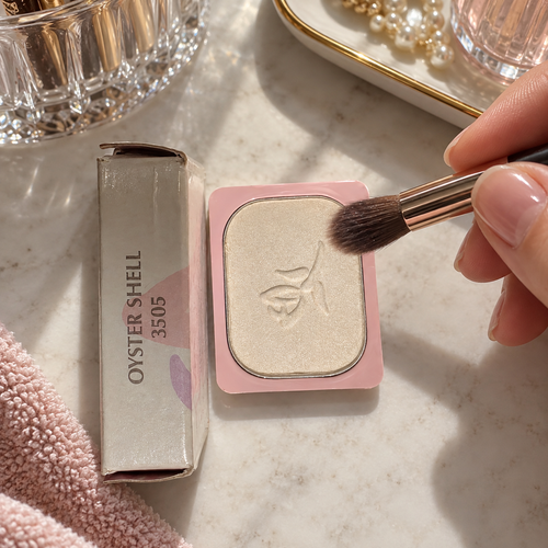 An eye-shadow brush beside the Oyster Shell refill in its pink rectangular holder