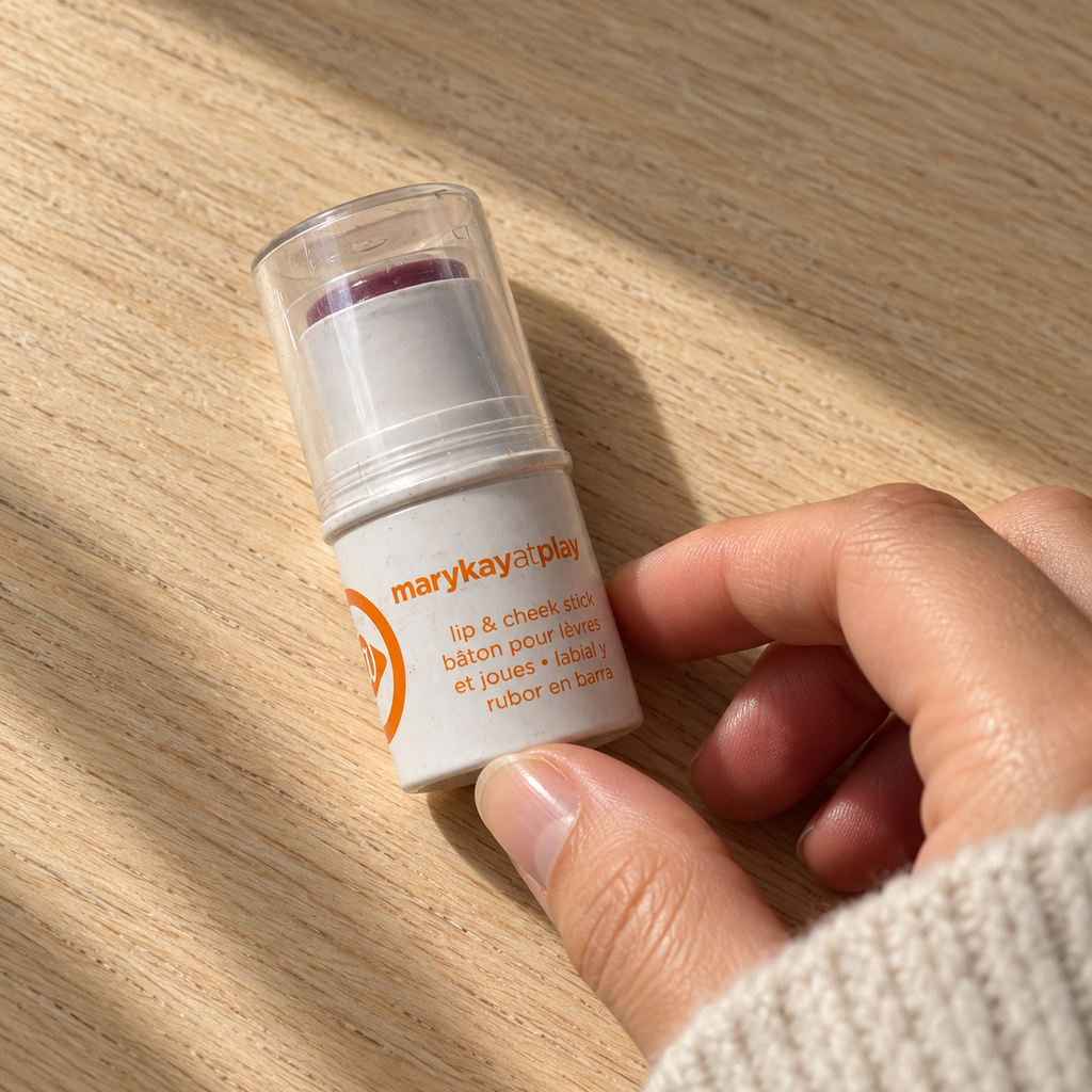 Hand reaching for Mary Kay at Play Razzleberry lip and cheek stick on a wooden tabletop