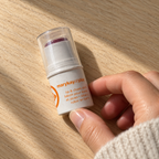 Hand reaching for Mary Kay at Play Razzleberry lip and cheek stick on a wooden tabletop