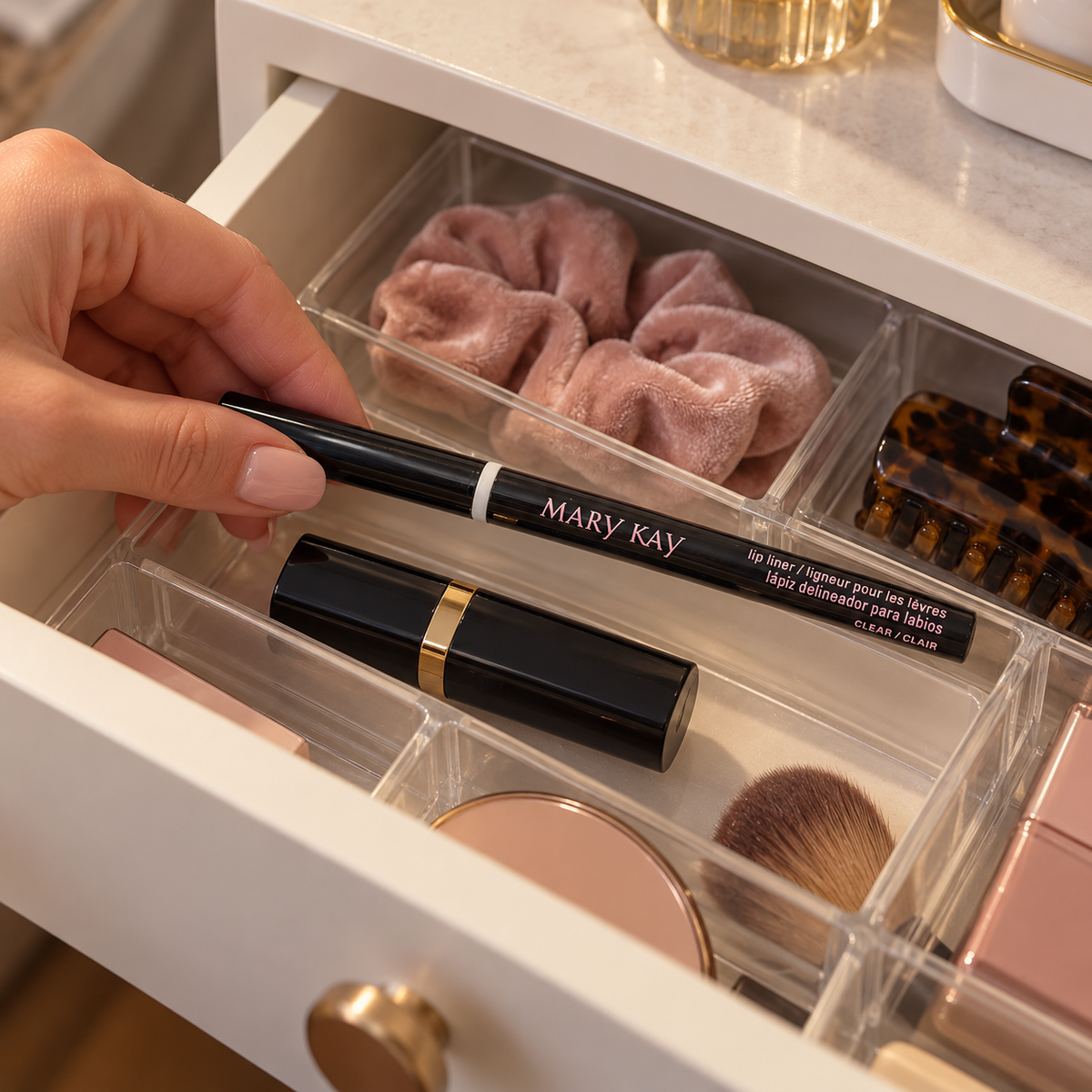 A hand places a capped black Mary Kay Clear lip liner in a vanity drawer organizer.