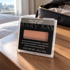 Mary Kay Sandstone mineral bronzing powder on a bedside table near a travel bag
