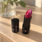 Mary Kay Empower Sparkle Cream Lipstick on a wooden dresser beside a glass vase