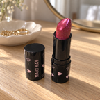 Mary Kay Empower Sparkle Cream Lipstick on an oak vanity beside a mirror and jewelry dish