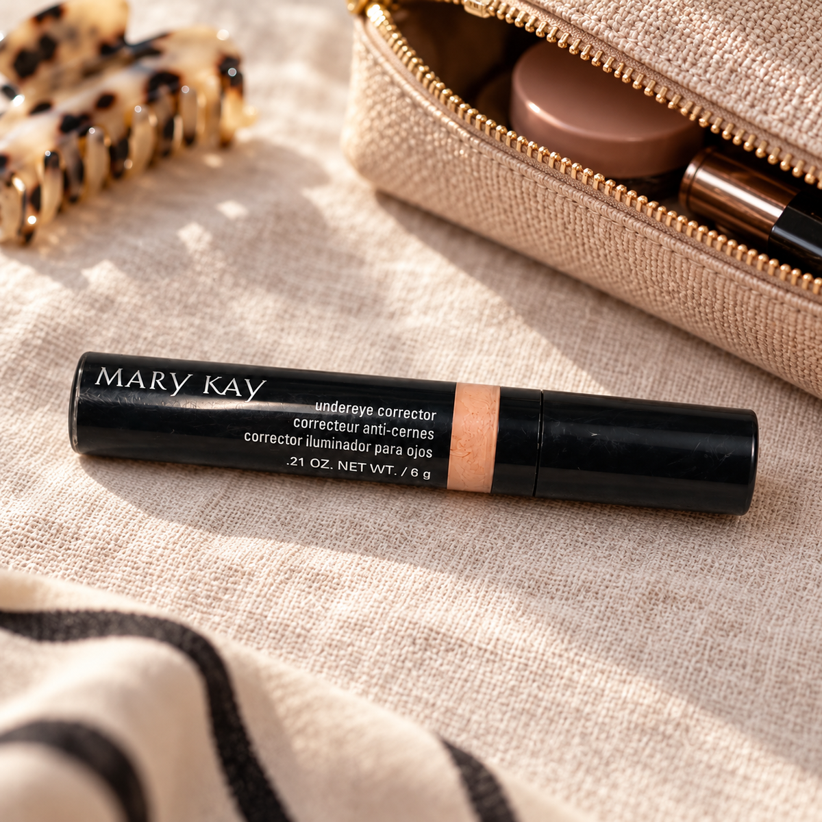 Mary Kay Undereye Corrector beside a beige makeup pouch on linen