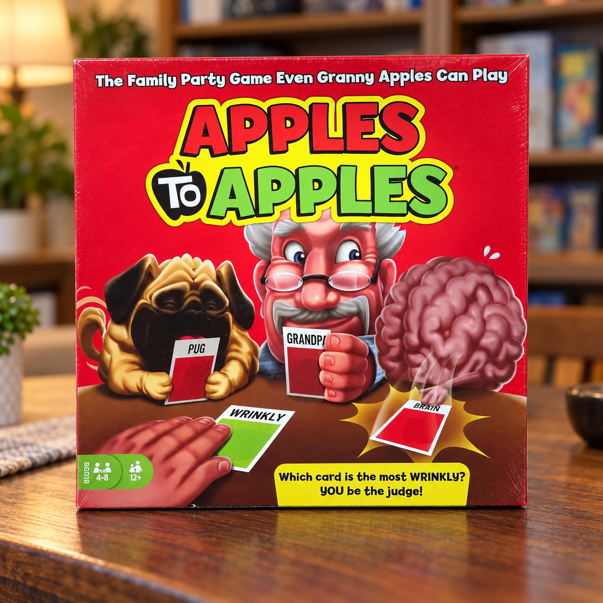 AI-generated lifestyle scene: closed Mattel Apples to Apples BGG15 game box on a recreation-room table; furnishings not included.