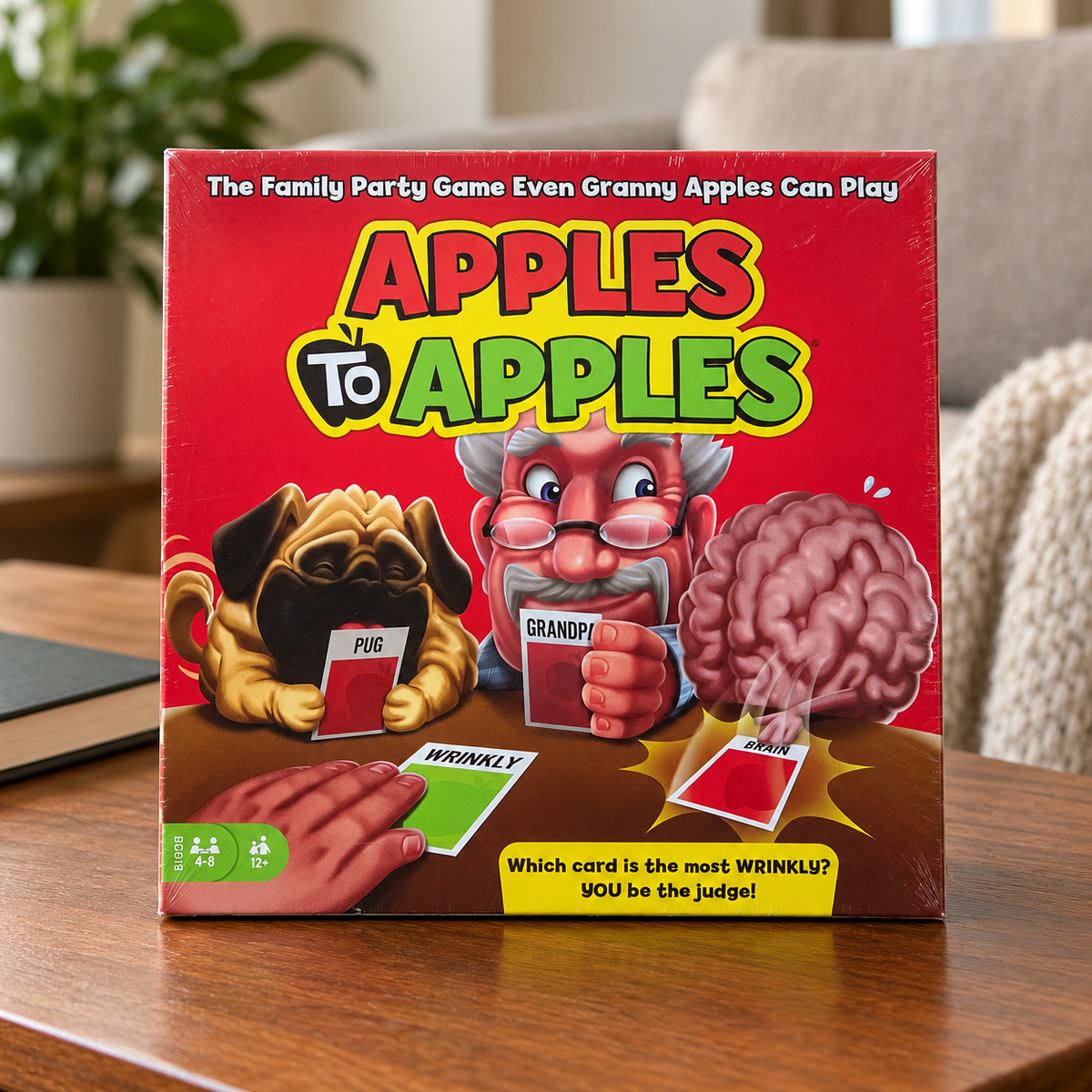 AI-generated lifestyle scene: closed Mattel Apples to Apples BGG15 game box on a coffee table; furnishings not included.