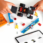 Hands assembling the MEGA Bone Shaker truck beside its course pieces and a tablet