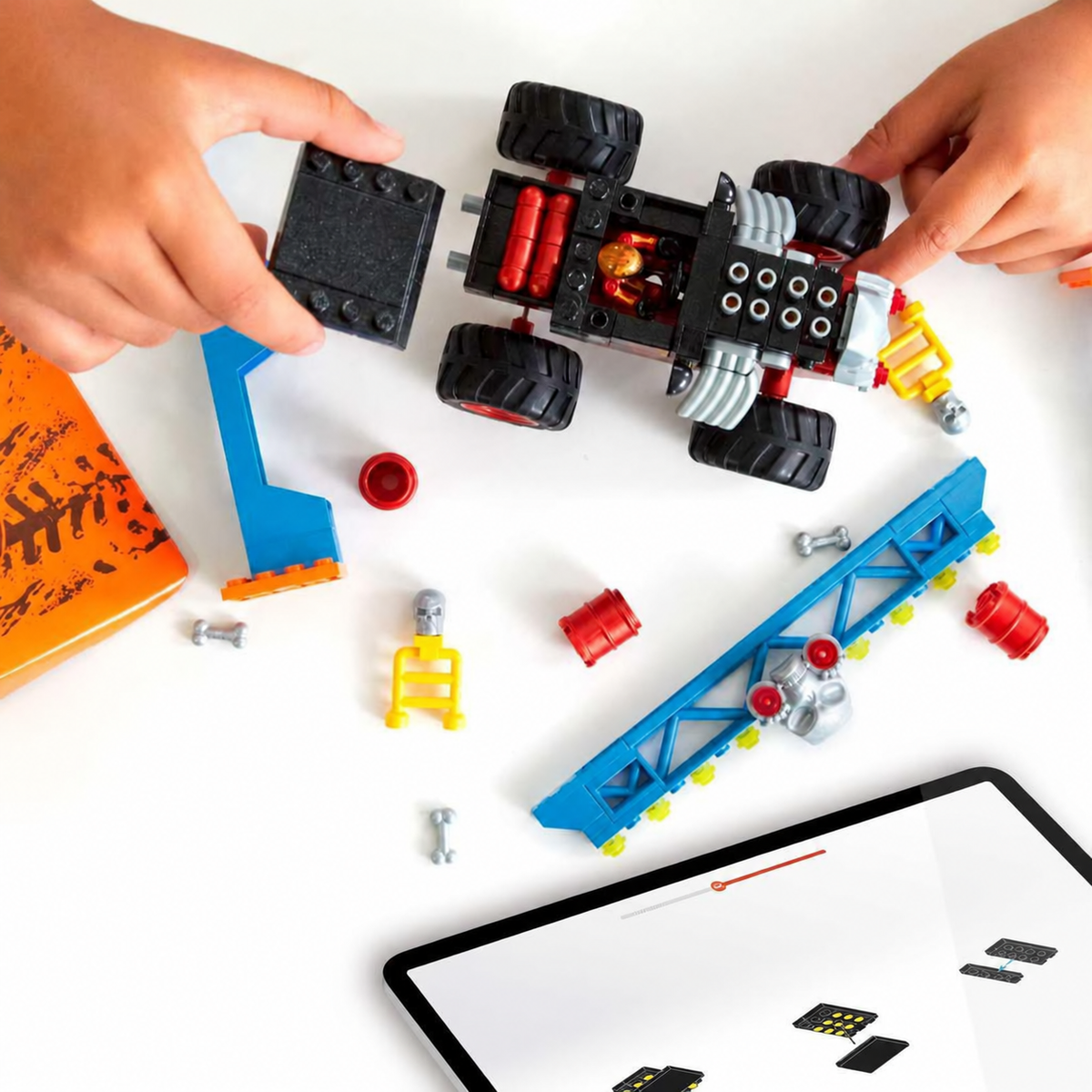Hands assembling the MEGA Bone Shaker truck beside its course pieces and a tablet