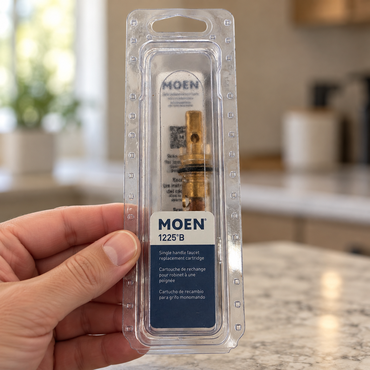 Adult hand holding the clear package of a Moen 1225B replacement cartridge.