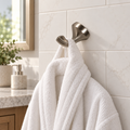 AI-generated bathroom scene of a brushed nickel robe hook holding a white towel on white tile.
