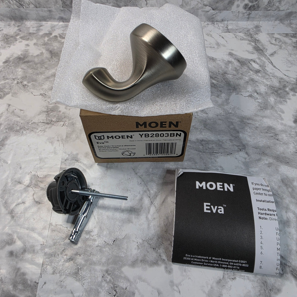 Actual stocked Moen Eva YB2803BN brushed nickel single robe hook with mounting hardware, box, and instruction booklet.